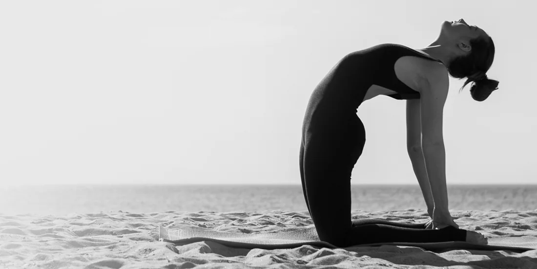 A woman stretching on a beach at dawn